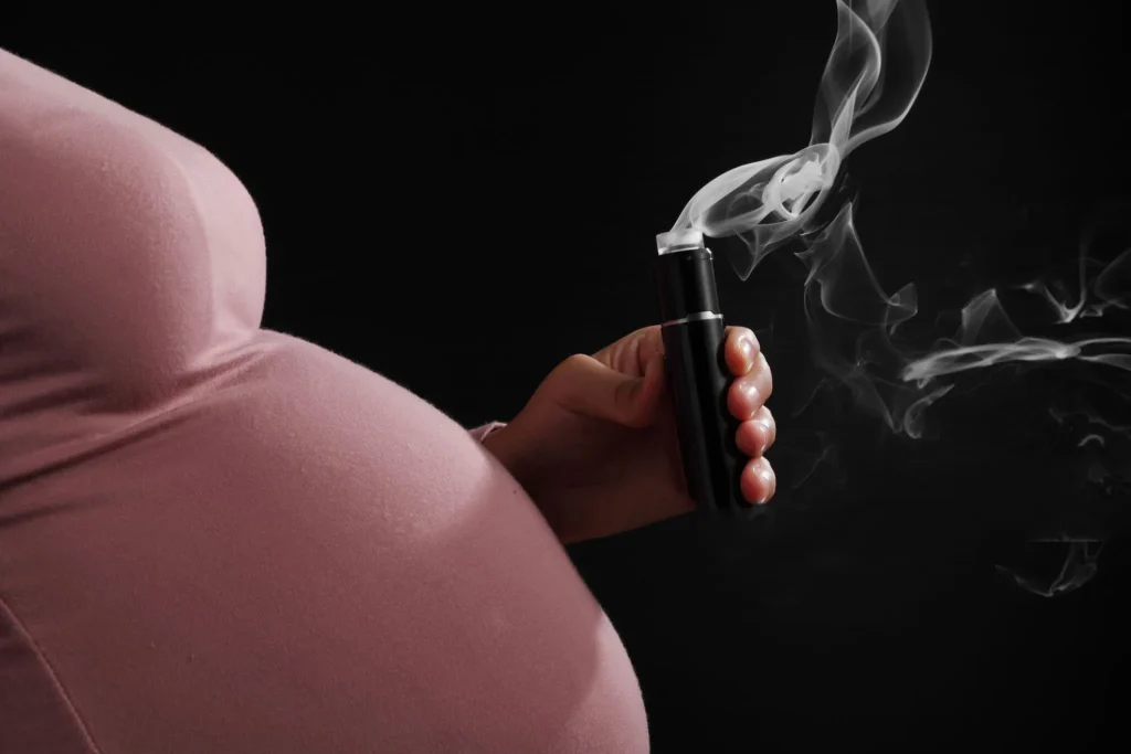 黑色背景下孕婦吸電子煙的特寫